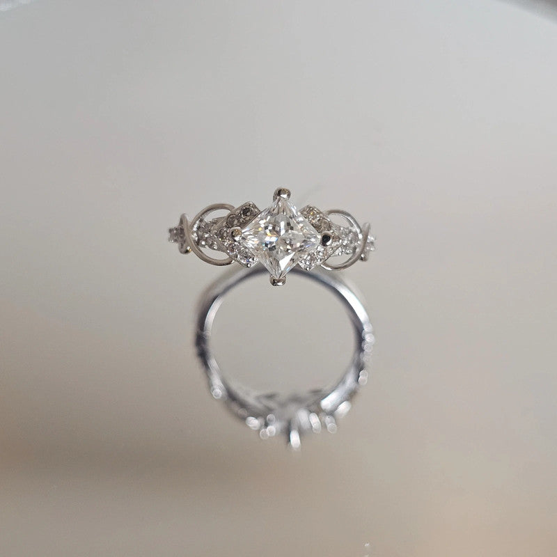 Side view of moissanite sterling silver ring with marquise accent stones and prong-set brilliant-cut center stone on reflective surface