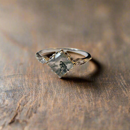 Elegant moss agate ring with square-cut gemstone and marquise side stones set in sterling silver sat on wooden surface