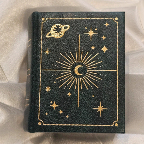 dark green book with gold celestial designs on a light fabric background
