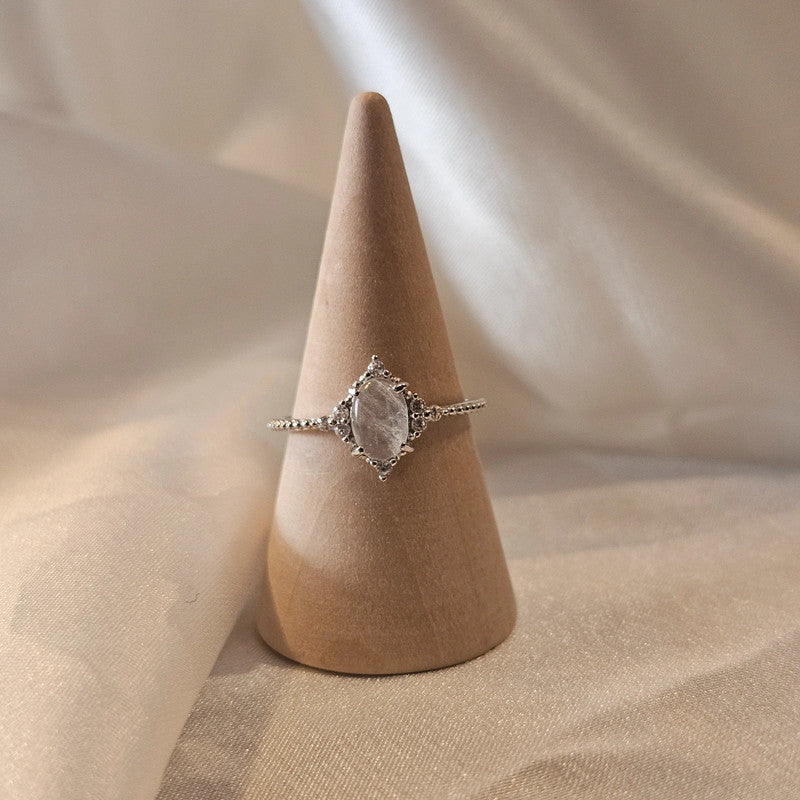 Silver natural moonstone ring with a stone on a wooden cone against a beige fabric background