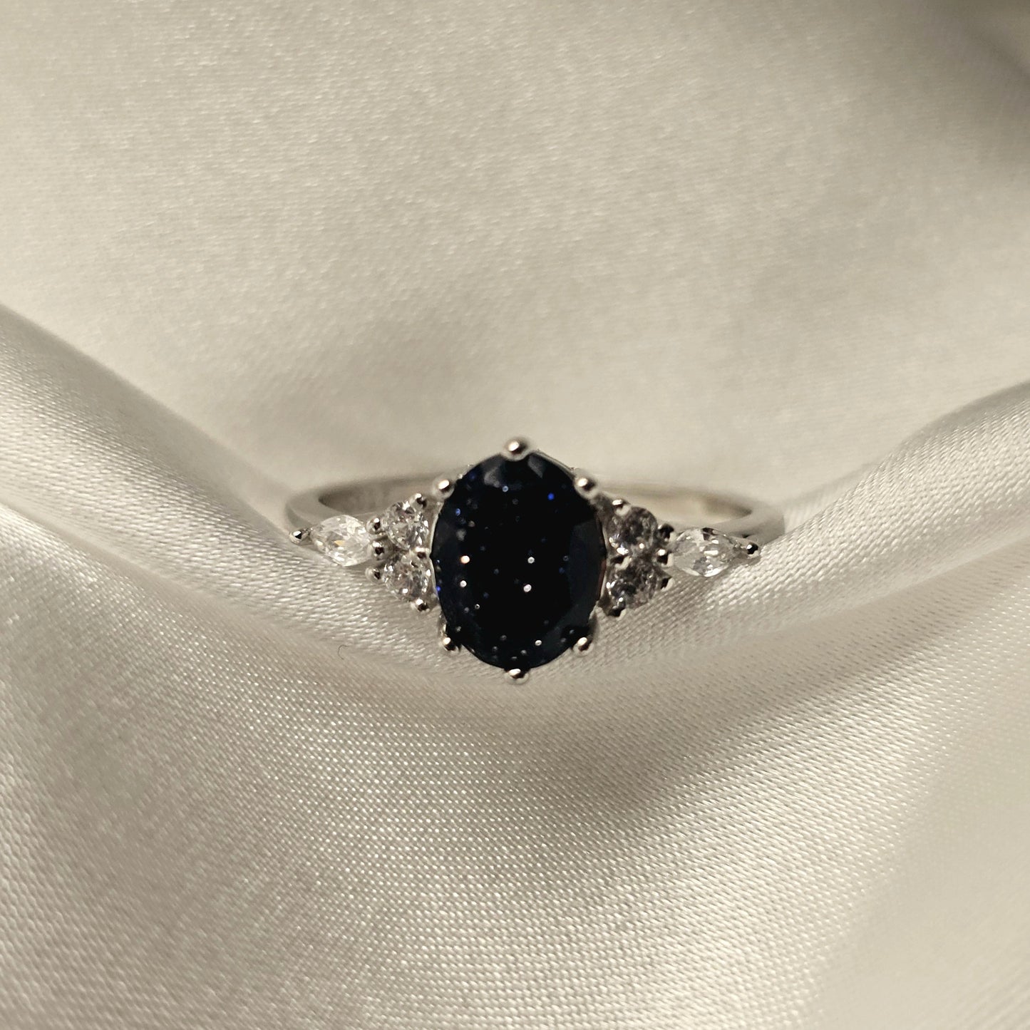Silver ring with a black gemstone on a white satin background