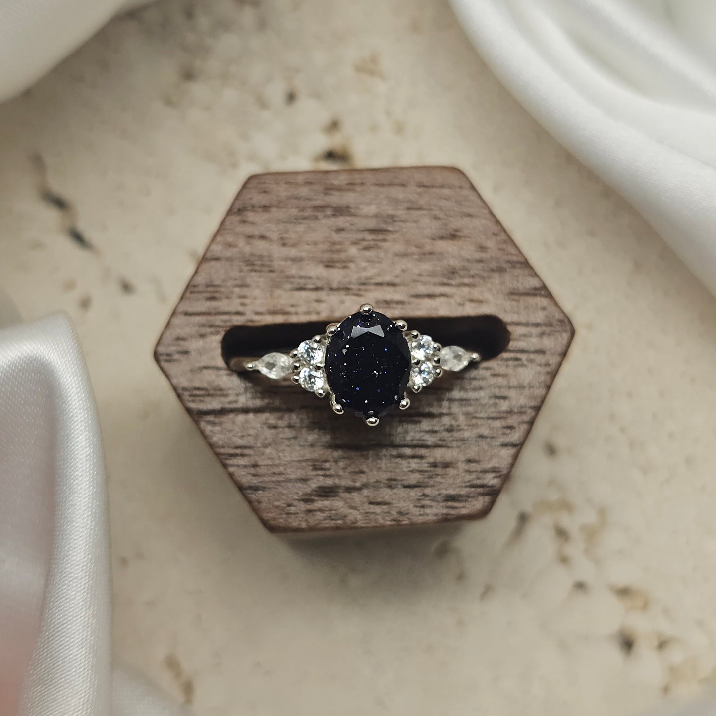 Ring with a black gemstone and diamond accents on a wooden hexagonal stand.