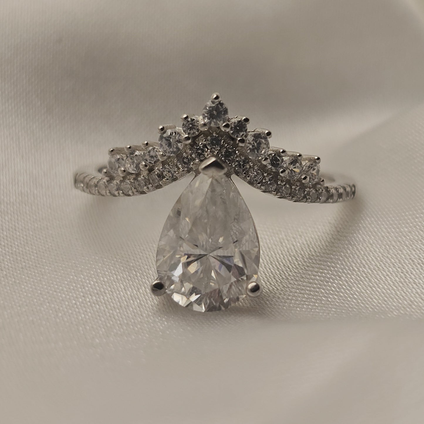 Diamond ring with a pear-shaped center stone on a light gray background