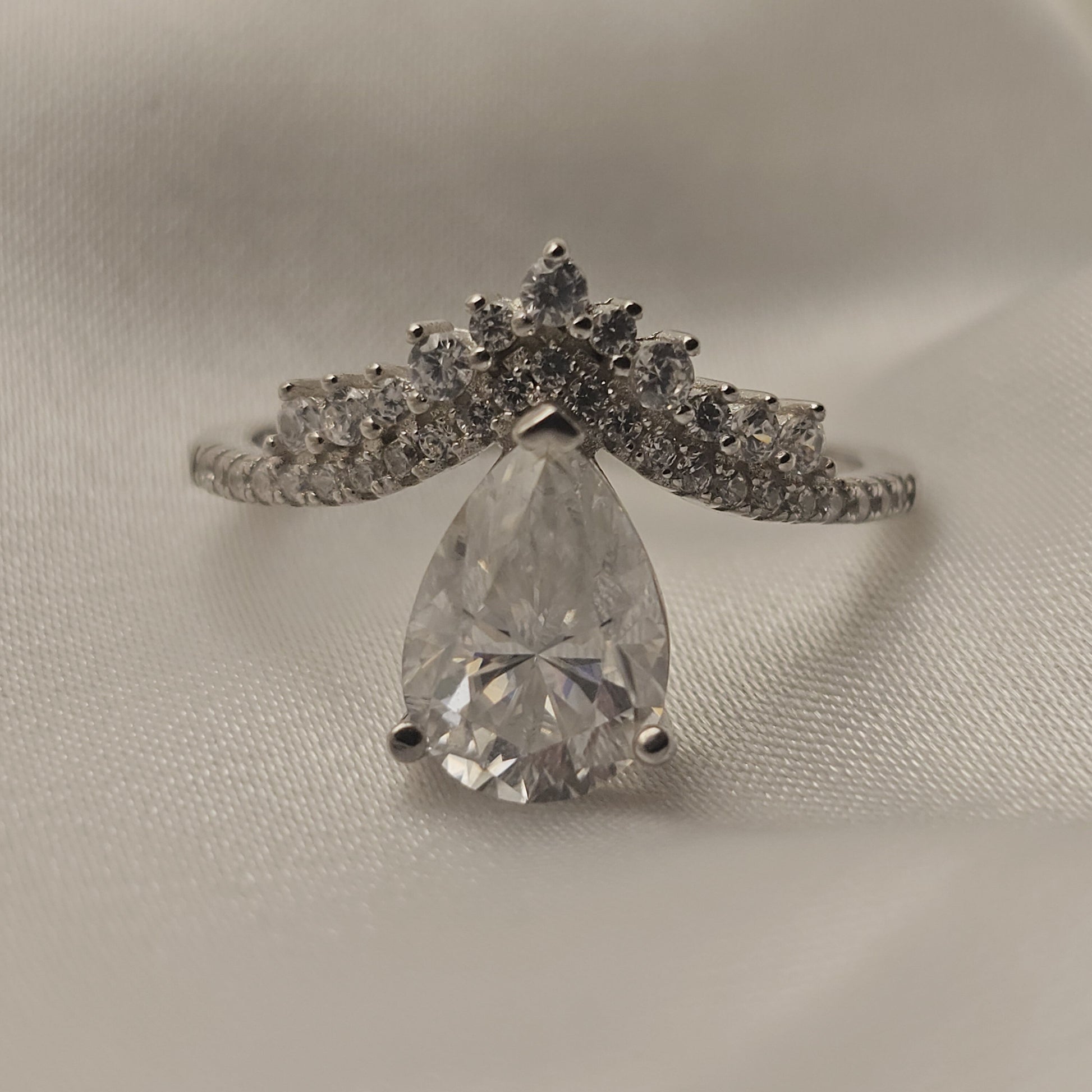 Diamond ring with a pear-shaped center stone on a light gray background