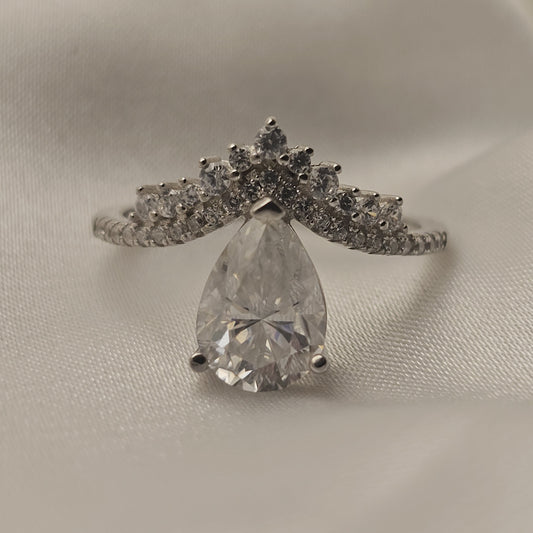 Diamond ring with a pear-shaped center stone on a light gray background