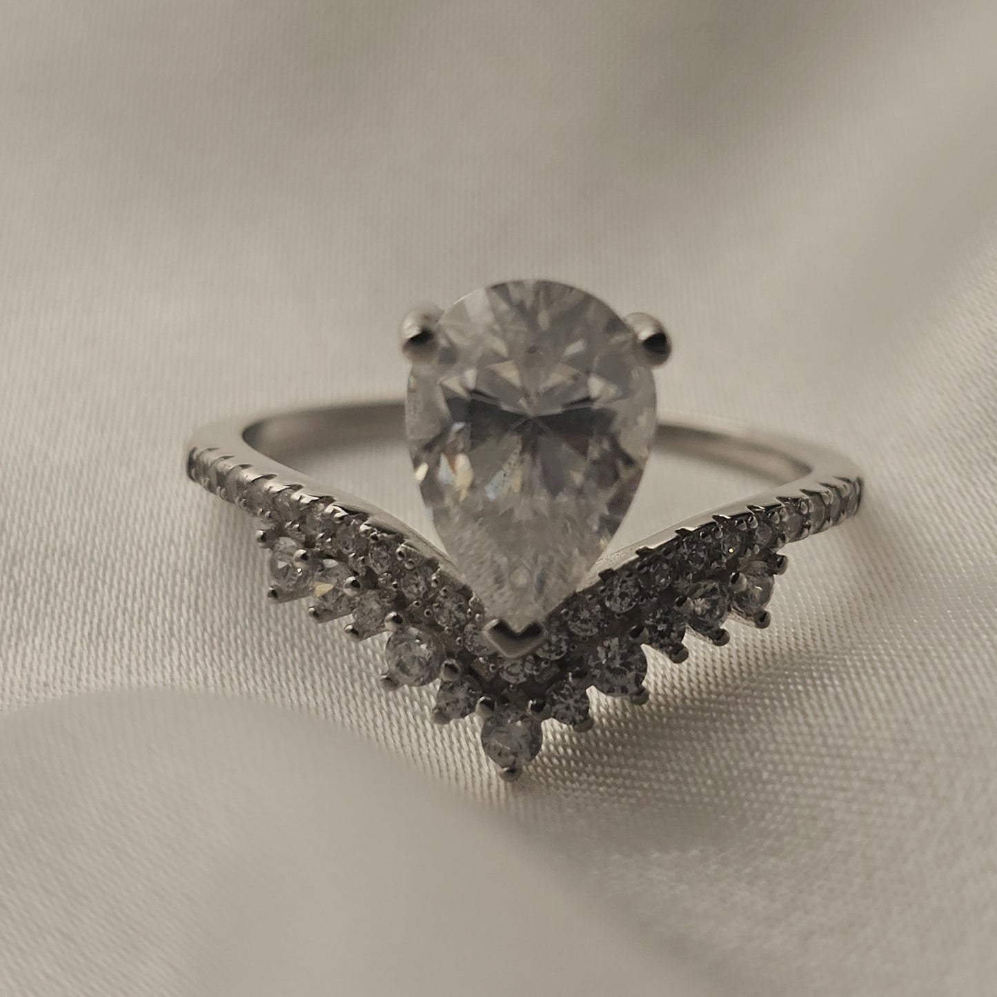 Silver ring with a large diamond and smaller diamonds on a beige fabric background