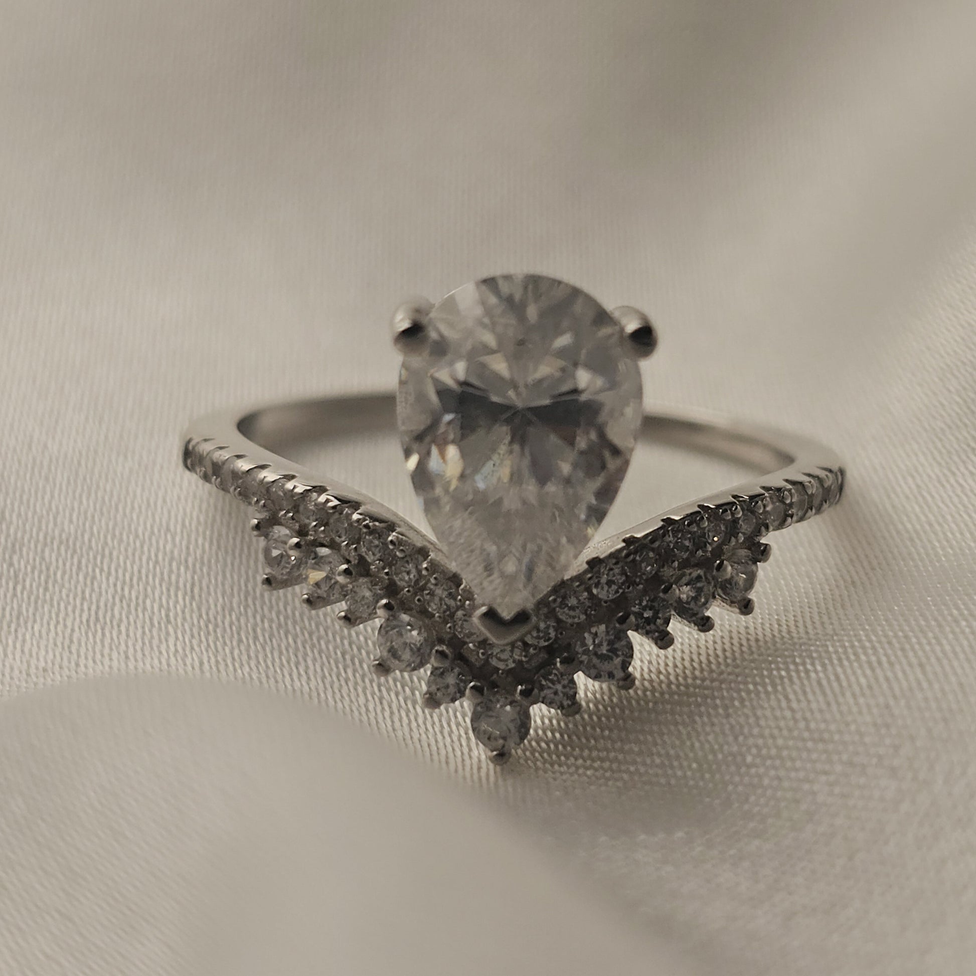 Silver ring with a large diamond and smaller diamonds on a beige fabric background