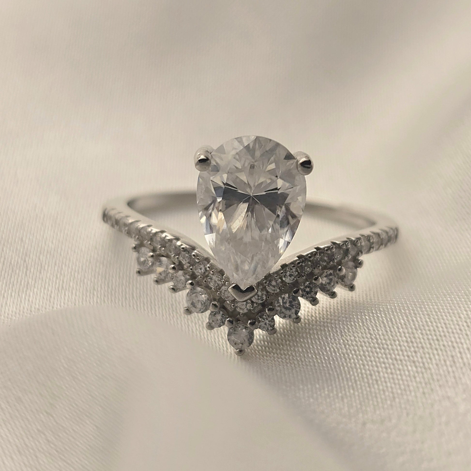 Diamond ring with a pear-shaped center stone on a light fabric background