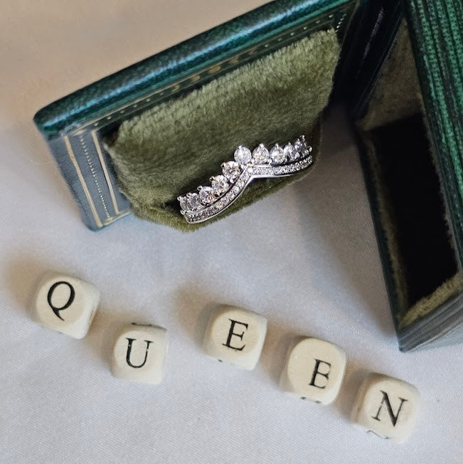 Diamond ring on a green jewelry box with 'QUEEN' spelled out using letter tiles.
