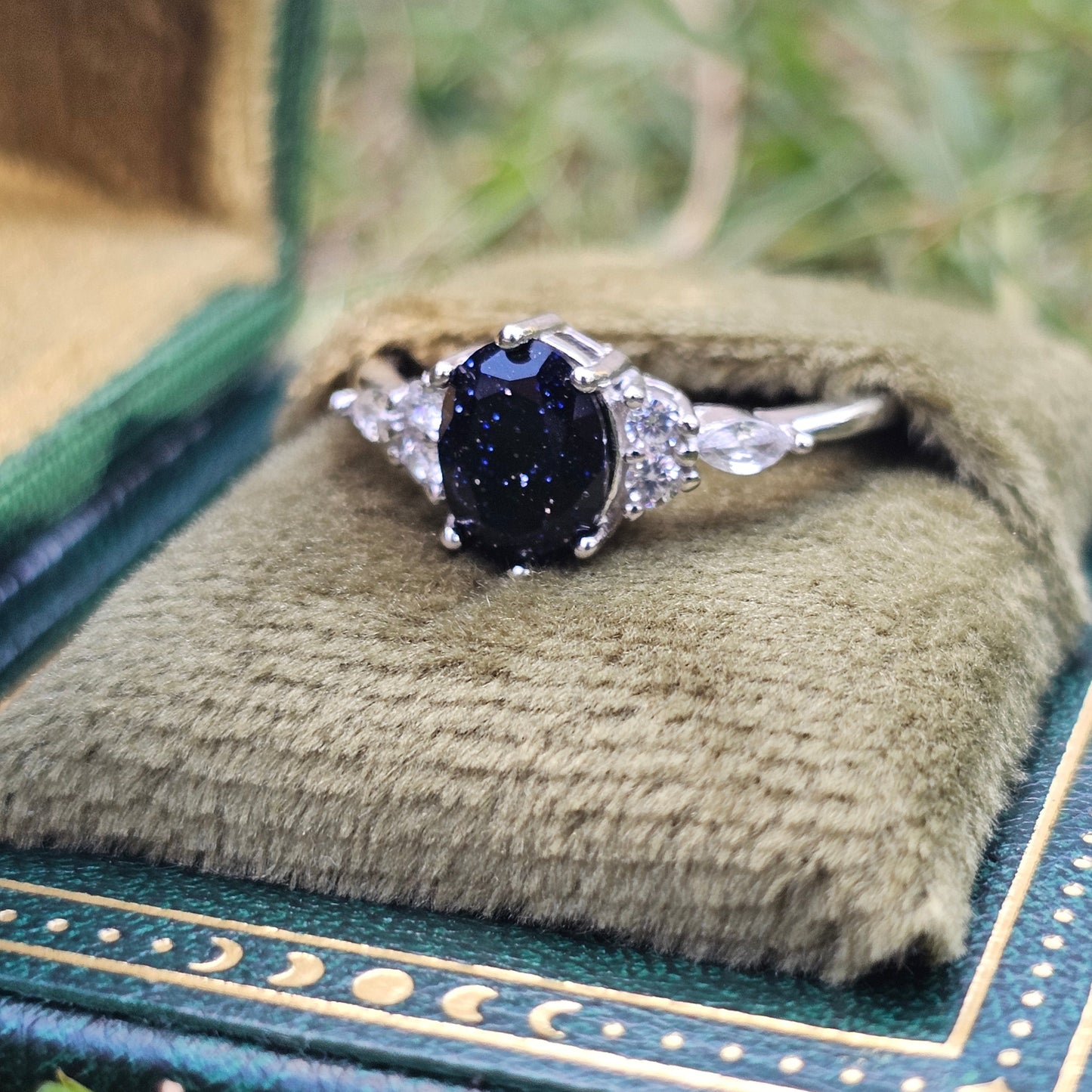Ring with a dark gemstone in a decorative box on grass