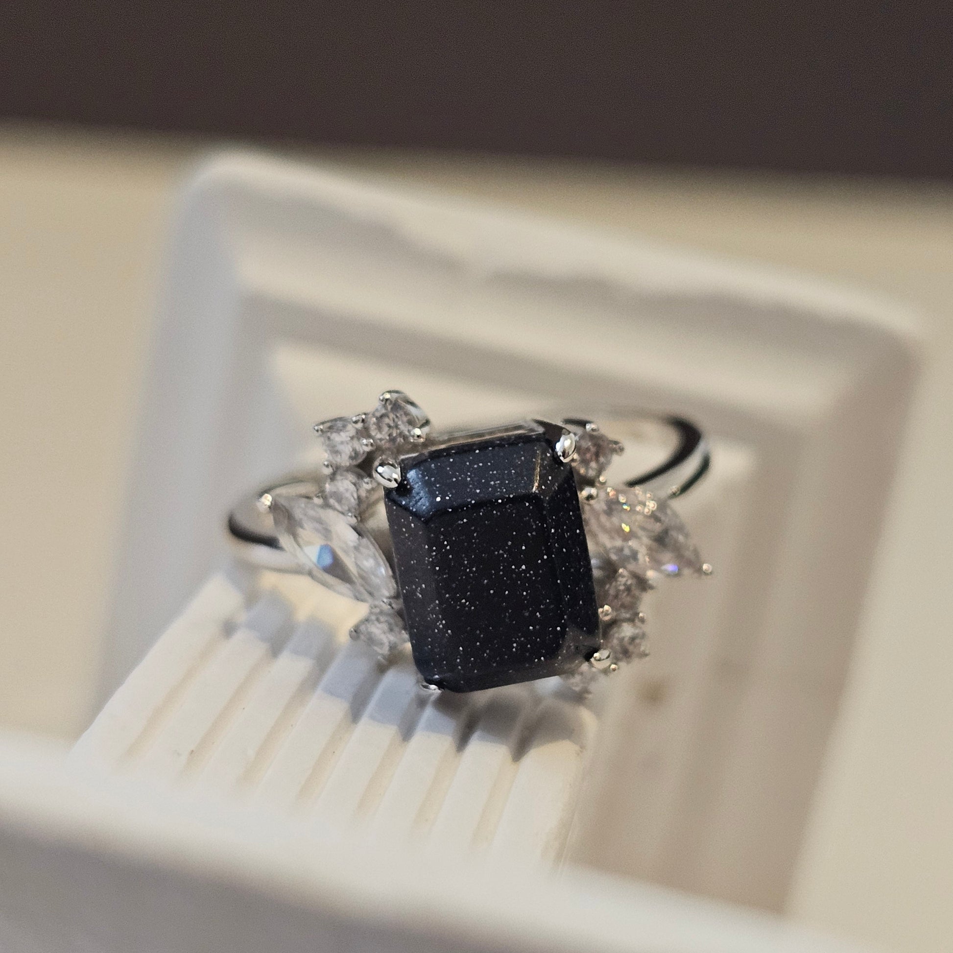 Ring with a black gemstone and diamond accents on a white stand.