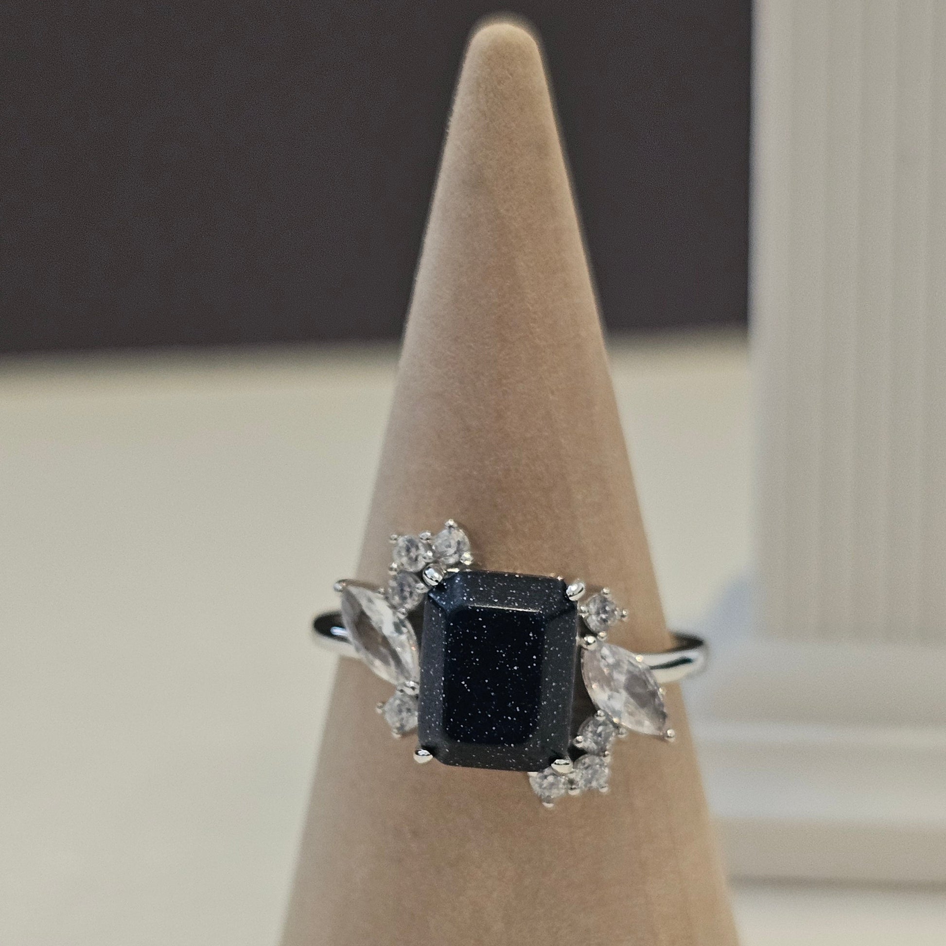 Black diamond ring on a beige stand against a neutral background