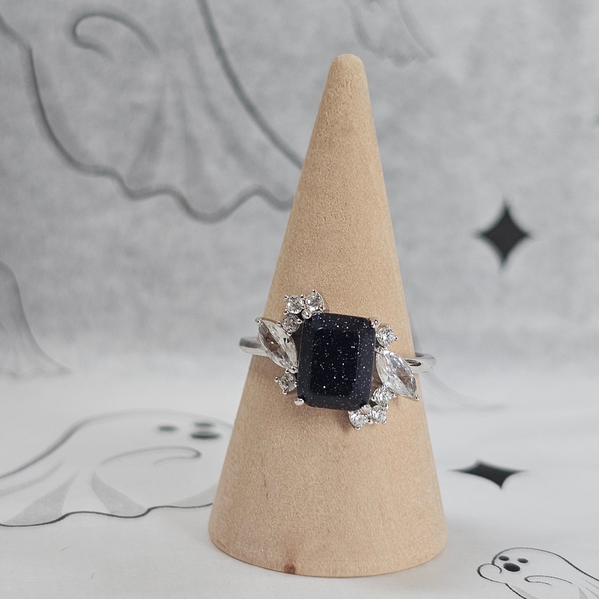 Ring with a black gemstone on a wooden cone against a patterned background