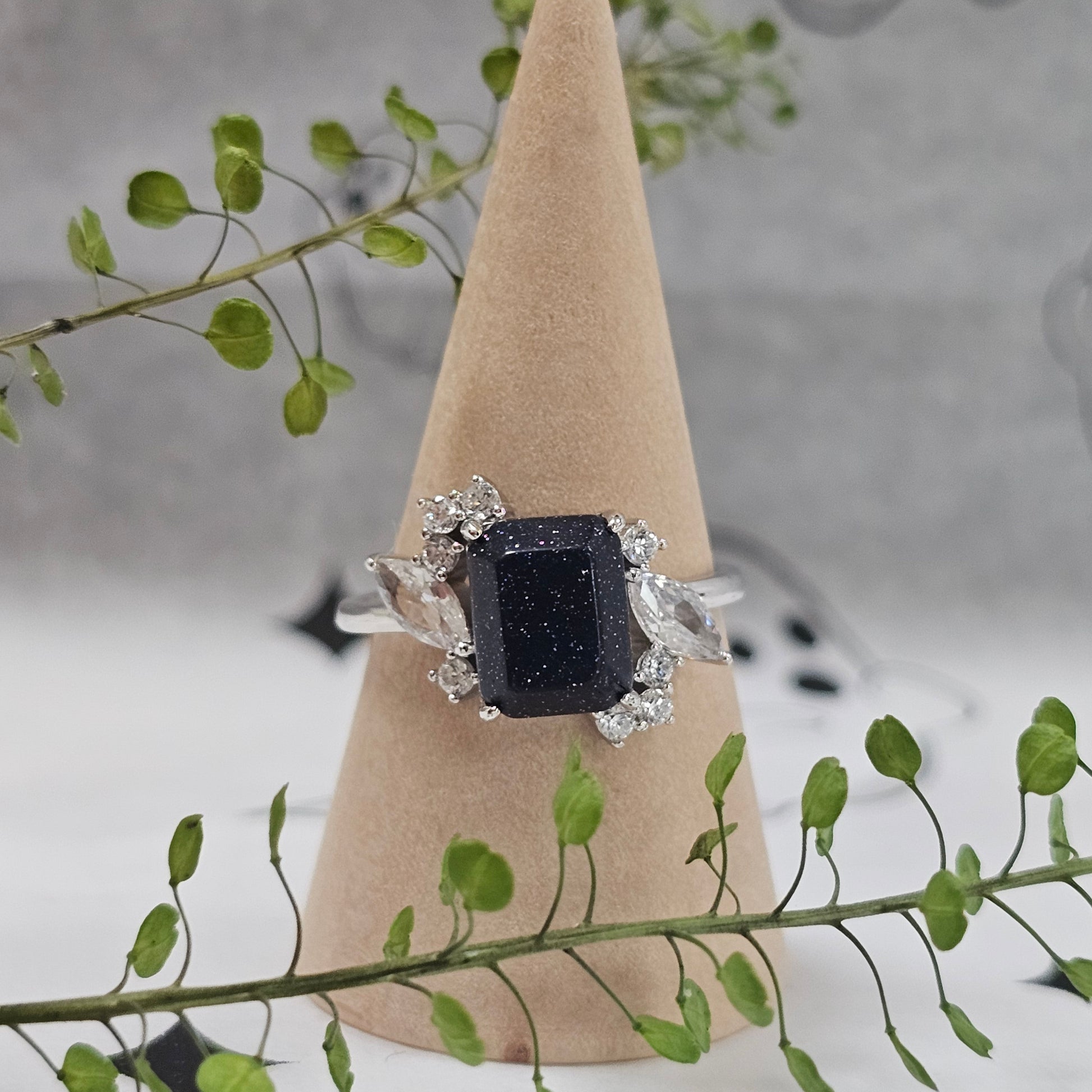Black square stone ring on a wooden stand with green leaves in the background