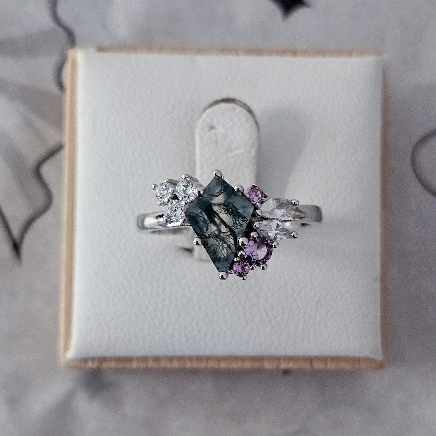 Silver ring with gemstones on a white cushion in a box