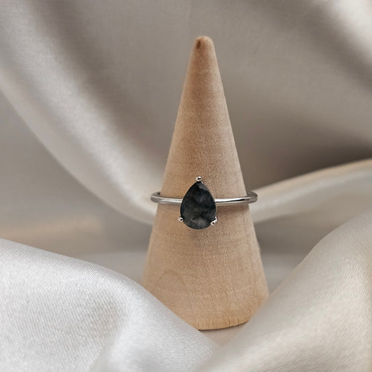 Ring with a black gemstone on a wooden stand against a neutral background