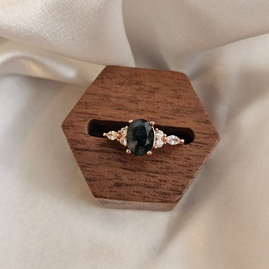 Earring with a moss agate gemstone and rose gold setting on a wooden stand against a beige fabric background
