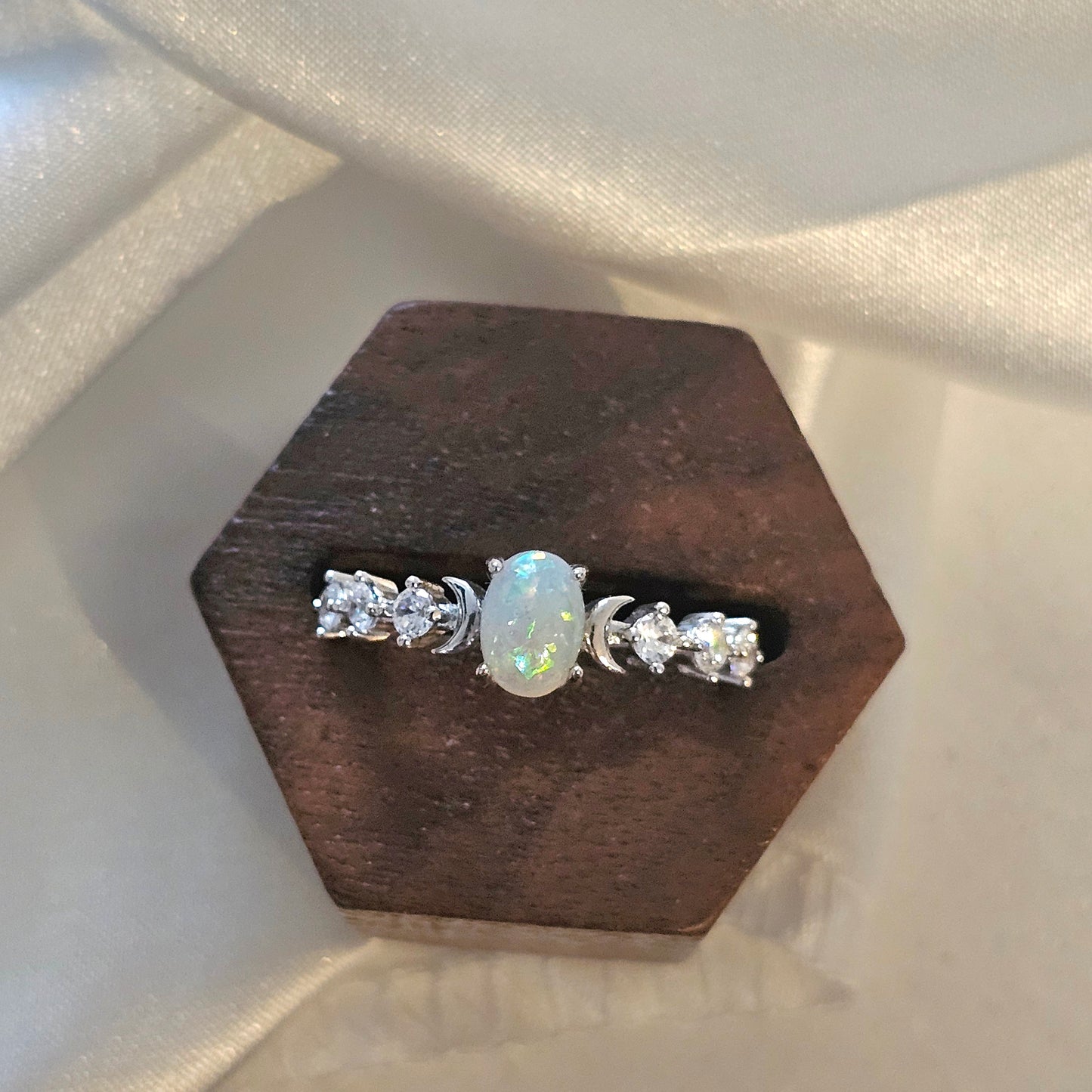 white opal  ring with a central gemstone on a wooden stand