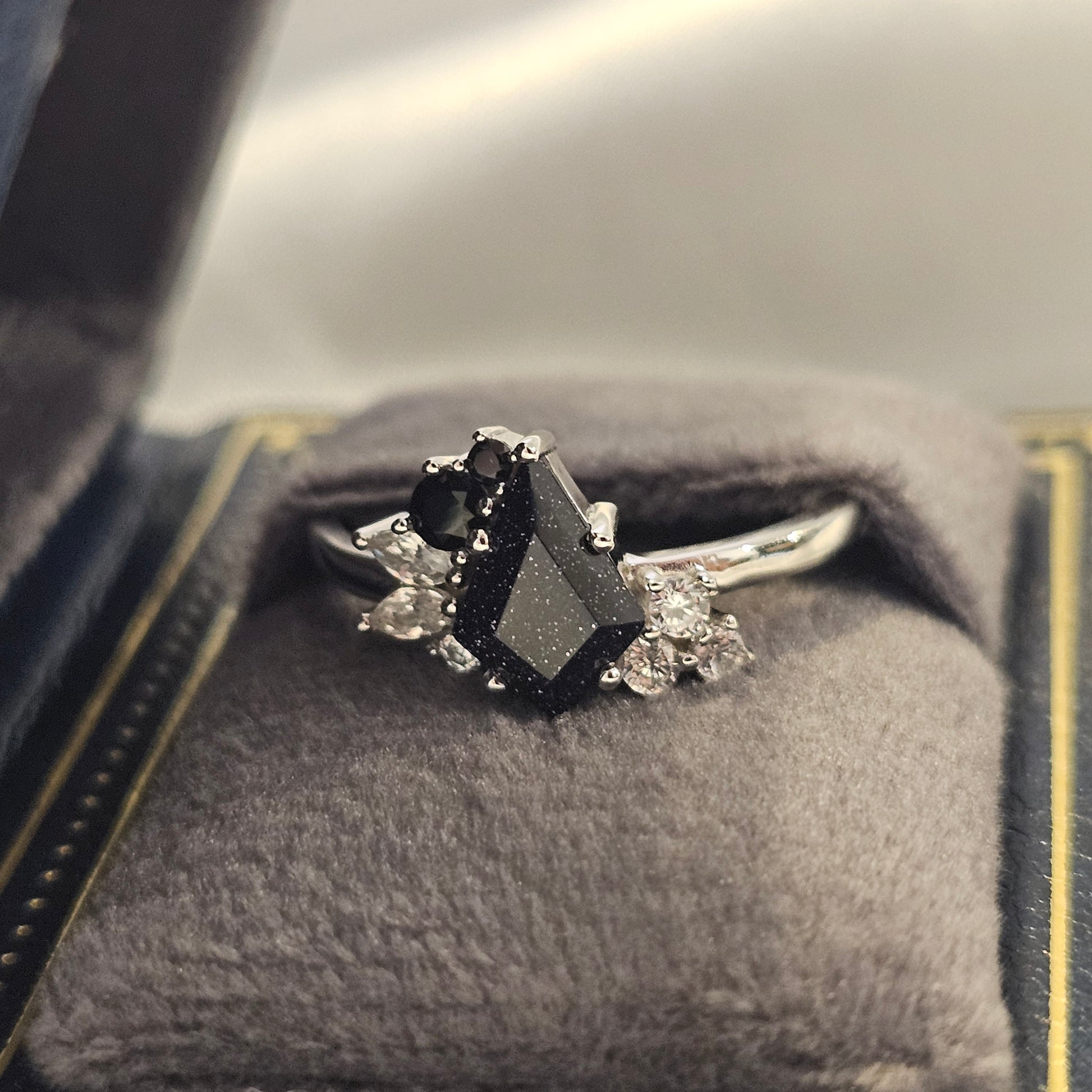 Silver ring with black gemstone and smaller diamonds on a textured surface