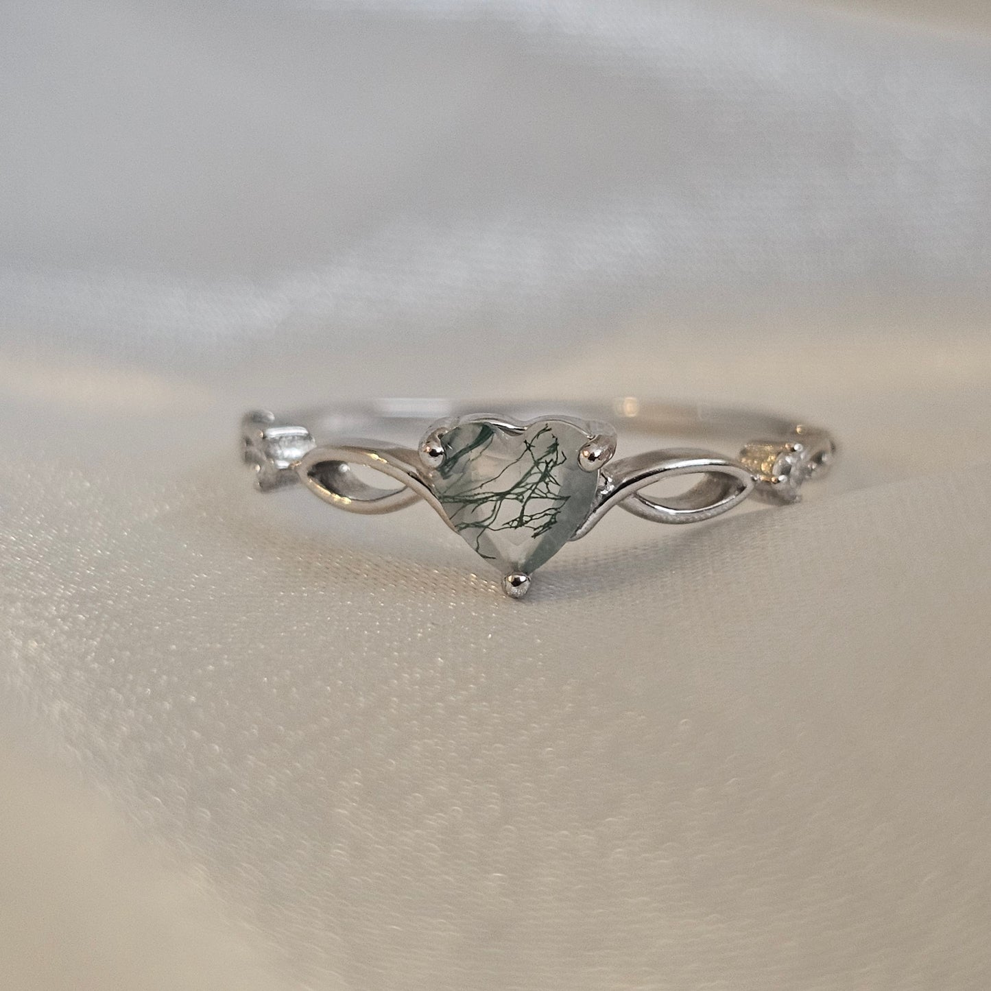 Natural Moss Agate heart-cut gemstone ring in sterling silver with infinity design — Evergreen Heart Ring on satin background.