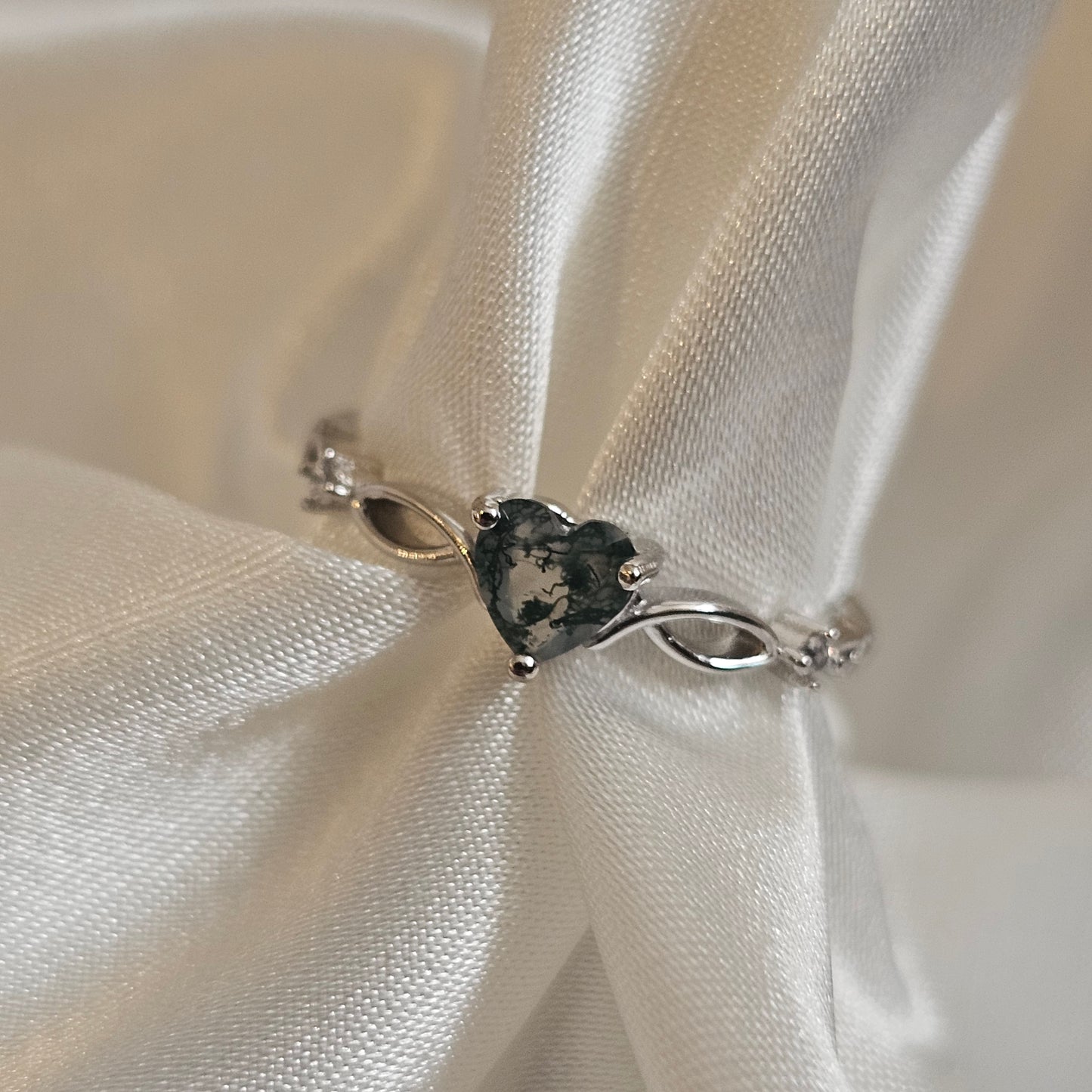 Natural Moss Agate heart-cut gemstone ring in sterling silver with infinity design — Evergreen Heart Ring on satin background.