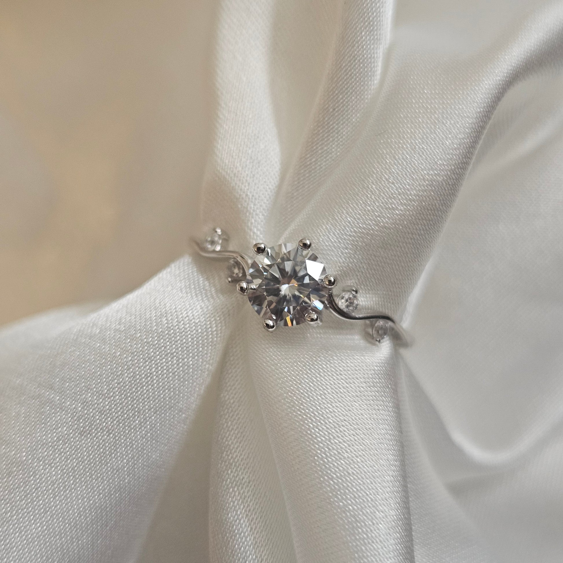 Moissanite engagement ring with twisting vine band and round brilliant-cut centre stone displayed on silk background