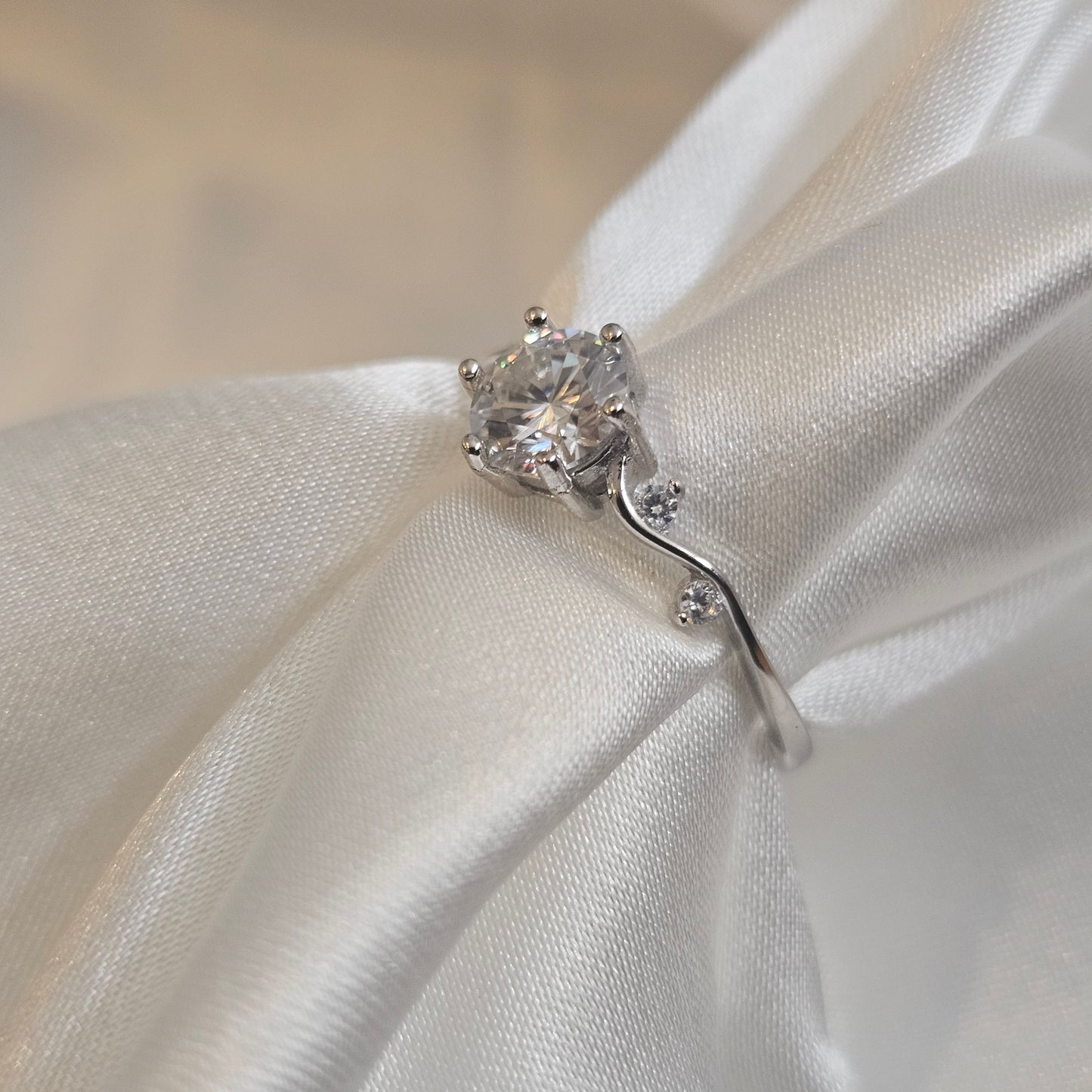Moissanite engagement ring with twisting vine band and round brilliant-cut centre stone displayed silk sheet