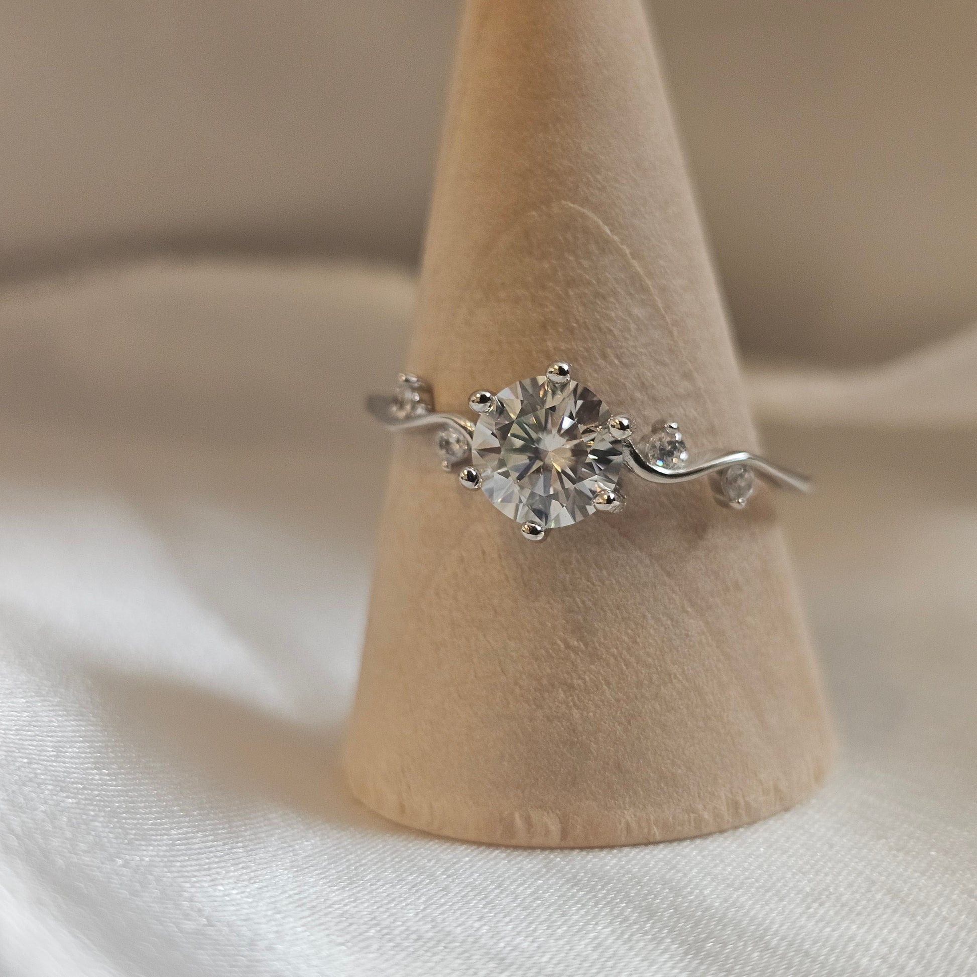 Silver ring with a large diamond on a beige stand against a white fabric background