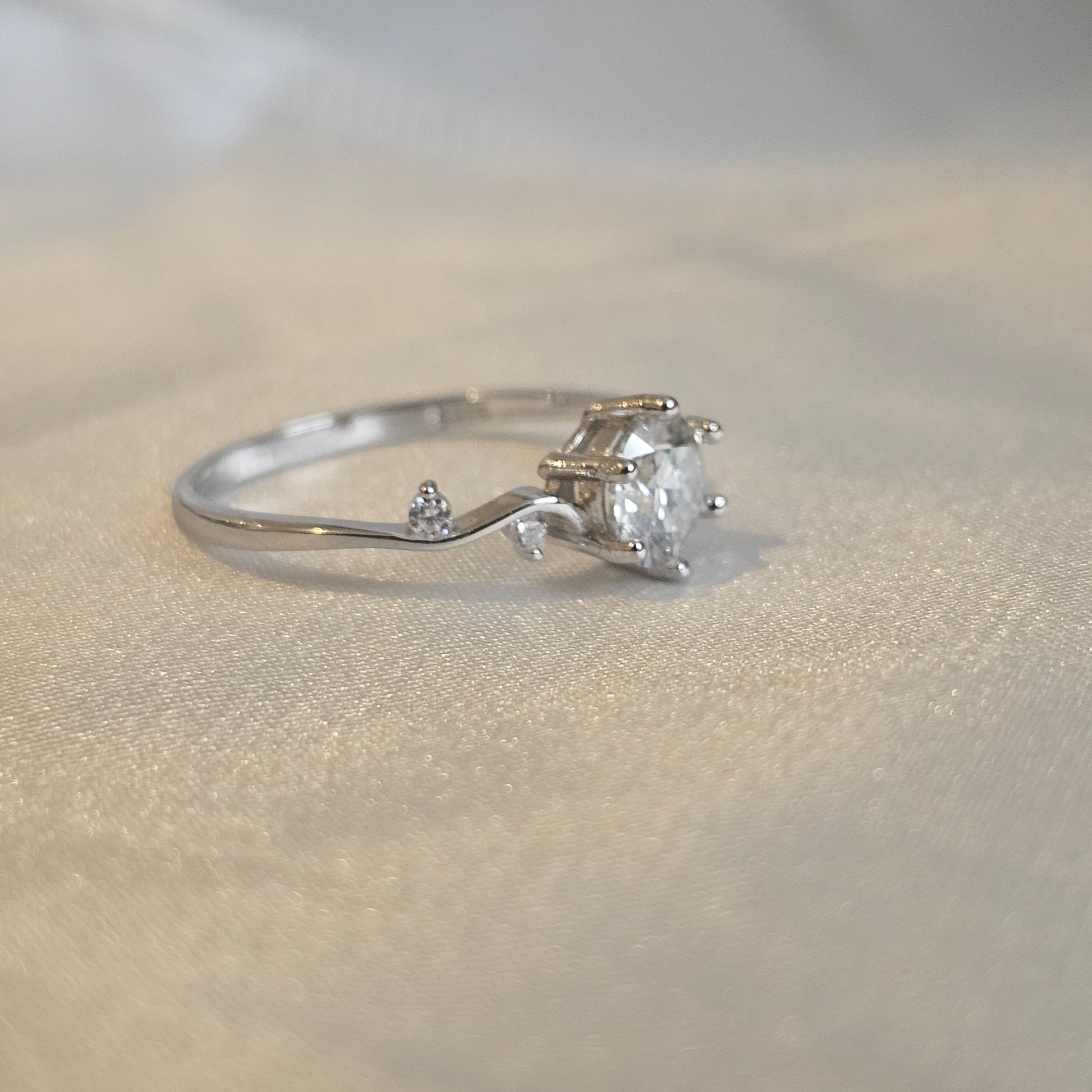 Moissanite engagement ring with twisting vine band and round brilliant-cut centre stone displayed silk sheet