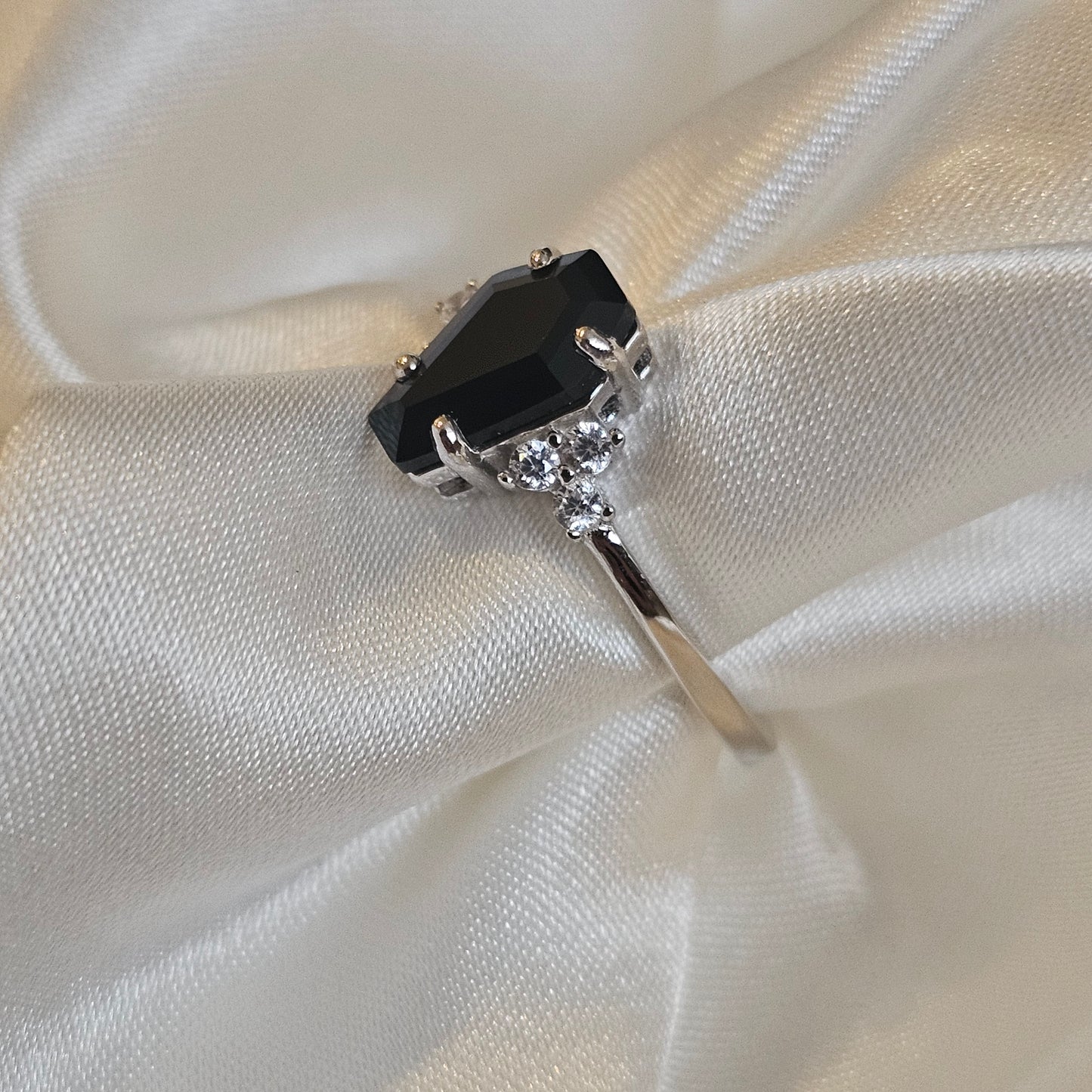 Silver ring with a black gemstone on white fabric