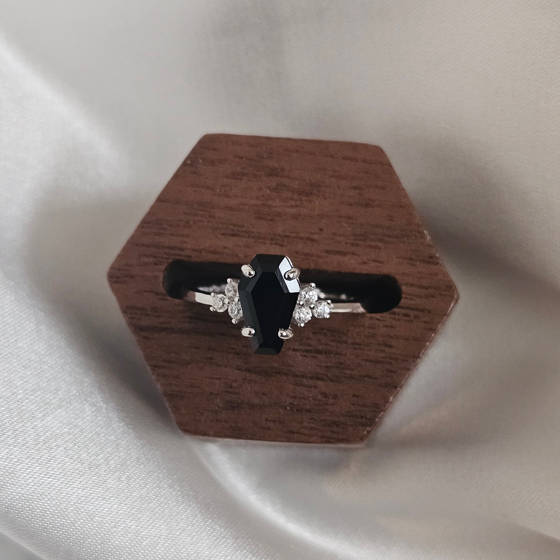 Black onyx ring on a wooden stand against a light fabric background