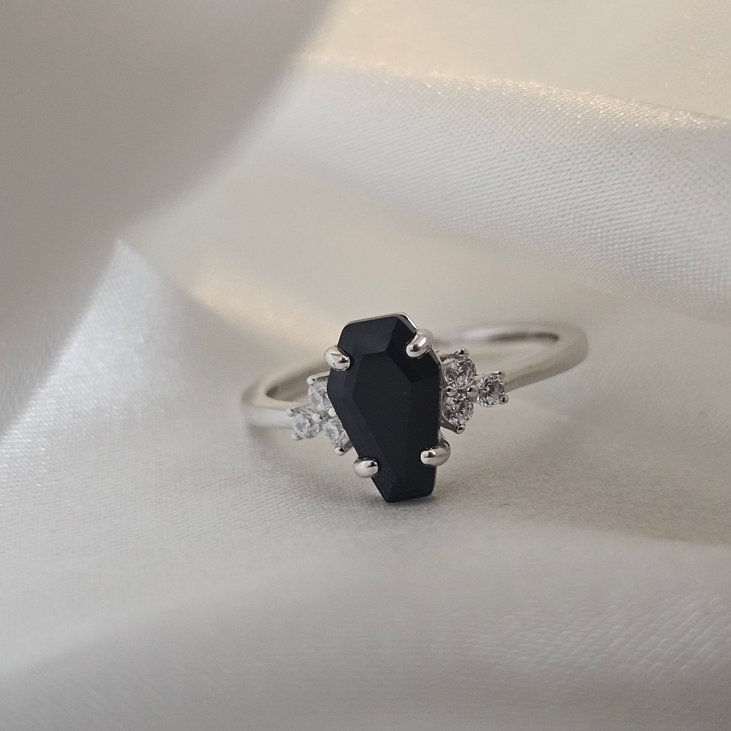 Silver ring with a black onyx gemstone and smaller diamonds on a white fabric background