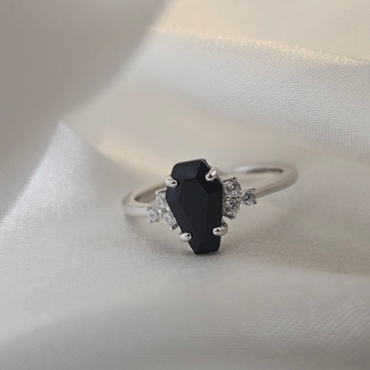 Silver ring with a black onyx gemstone and smaller diamonds on a white fabric background