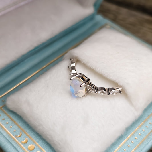 Lab-created moonstone ring in 925 sterling silver displayed in a celestial book-style ring box with light blue exterior, gold detailing, and soft faux fur lining.