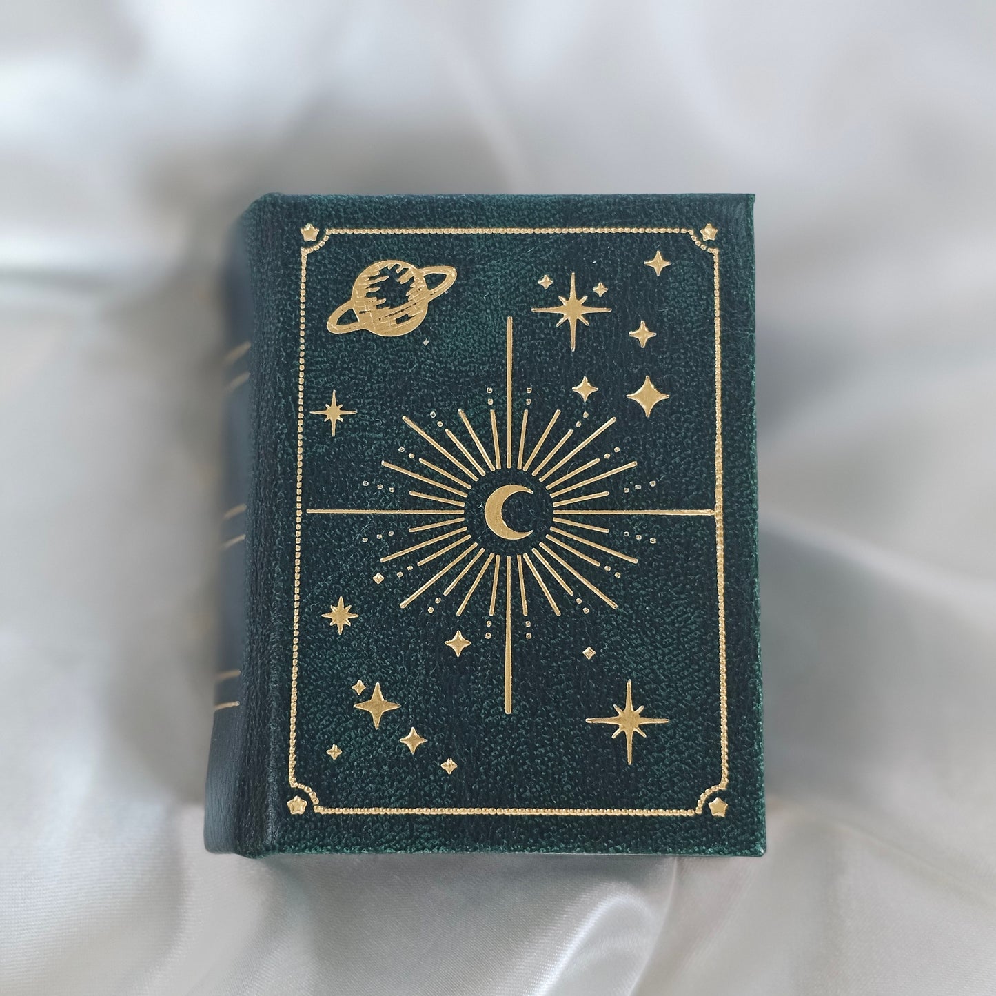 Dark green book with gold celestial designs on a white fabric background