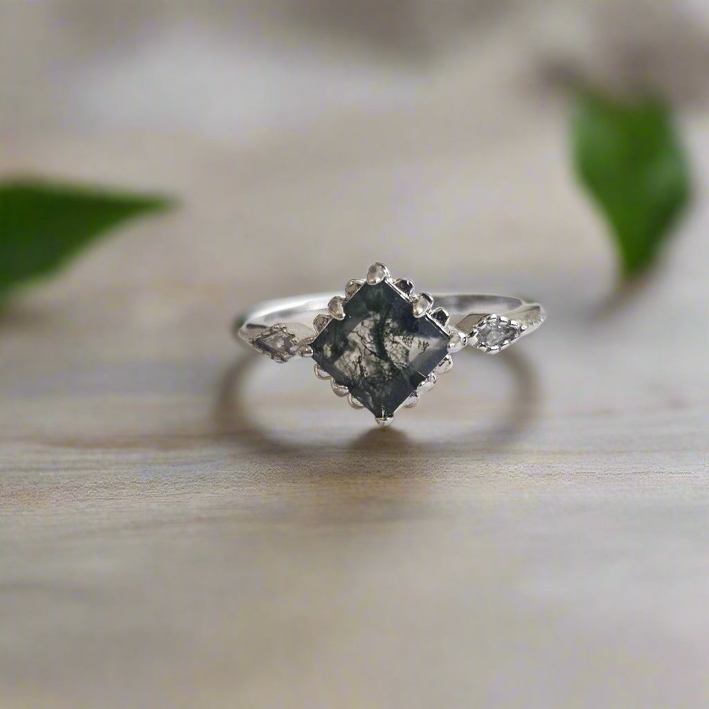 Silver ring with square moss agate stone on wooden surface