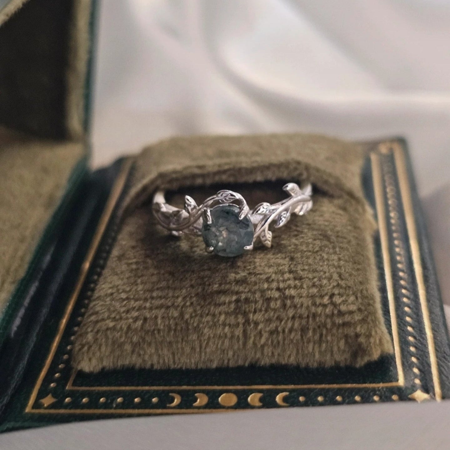 Silver ring with a green gemstone in a decorative box