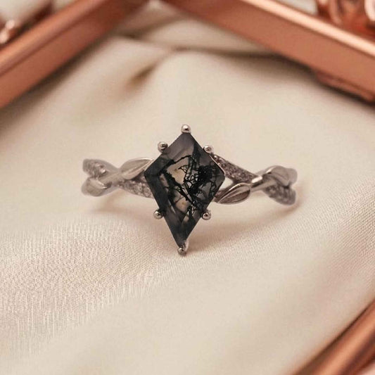 Close-up of kite cut Moss Agate ring in 925 sterling silver with 18k white gold plating and cubic zirconia accents, featuring leaf detail band on ivory fabric background