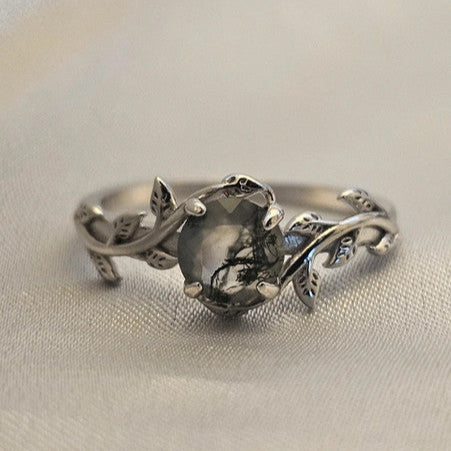 Moss agate ring 925 silver with leaf detail sat on a silk cloth
