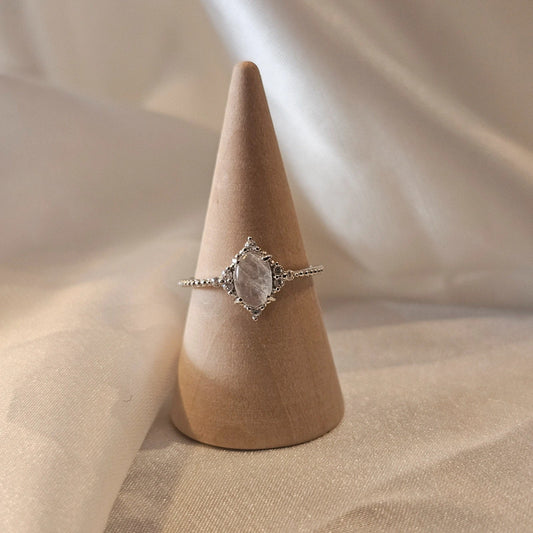 Silver natural moonstone ring with a stone on a wooden cone against a beige fabric background