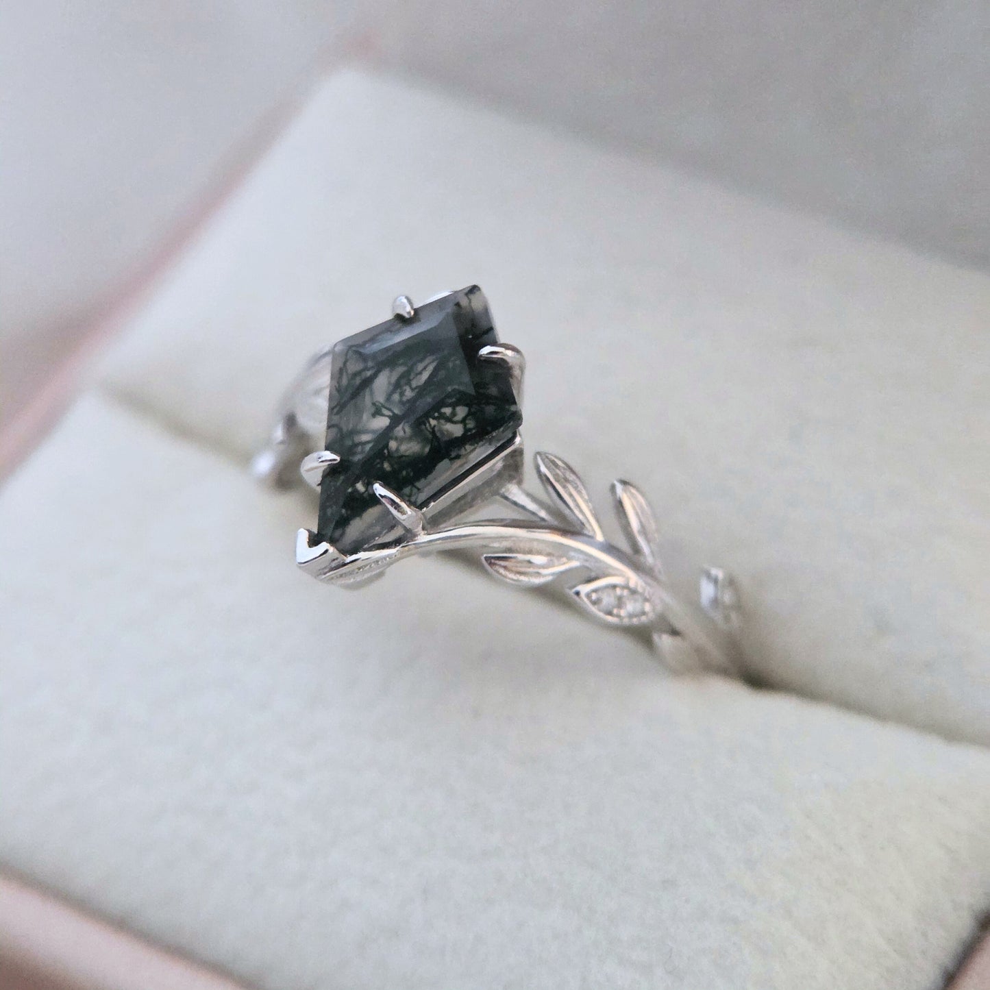 Olive Grove natural moss agate ring in 925 sterling silver with platinum plating, showing a square-cut green moss agate stone and leaf-inspired band resting on a soft cushion