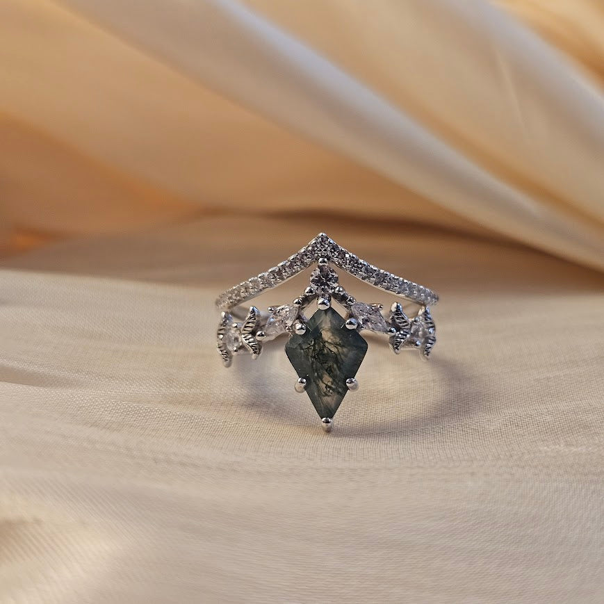 Moss agate engagement ring with crown-shaped band and marquise accent stones displayed on beige satin fabric background