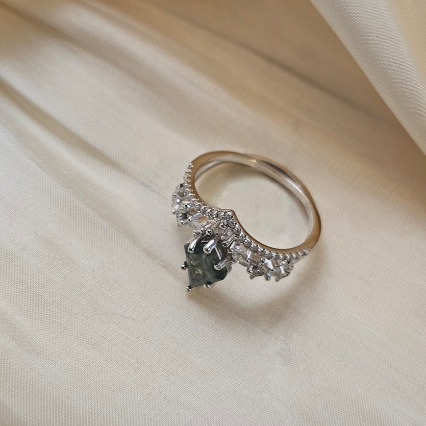 Moss agate engagement ring with crown band and sparkling accent stones displayed on beige satin fabric background