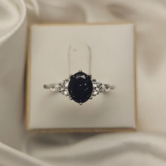 Ring with a black gemstone and silver accents on a white box