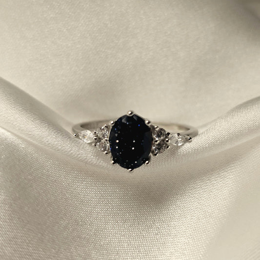 Silver ring with a black gemstone on a white satin background