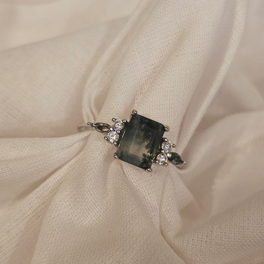 ring with a dark moss agate gemstone and smaller stones on beige fabric