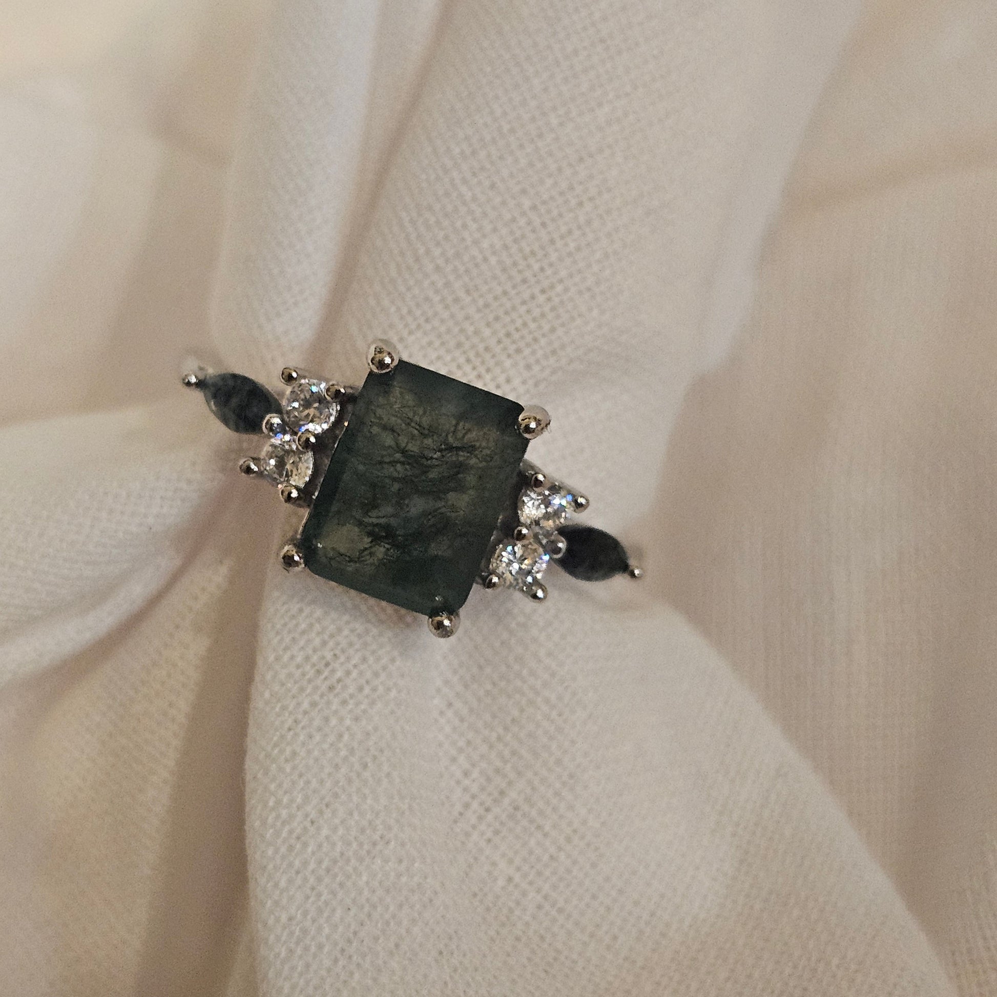 Silver ring with a large central stone and smaller stones on a beige fabric background