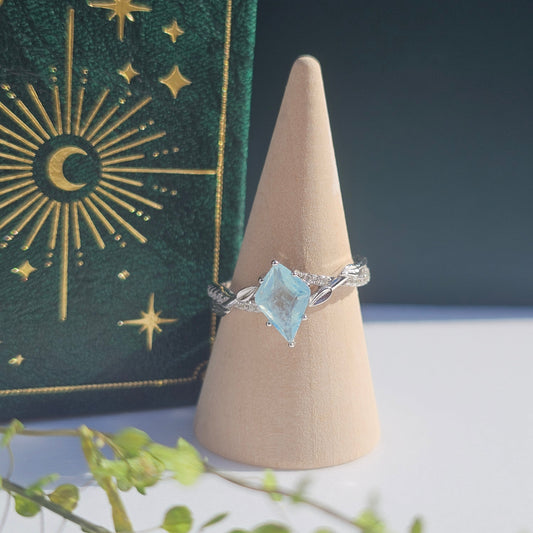 Silver ring with a blue gemstone on a beige stand against a dark background with star and moon designs.