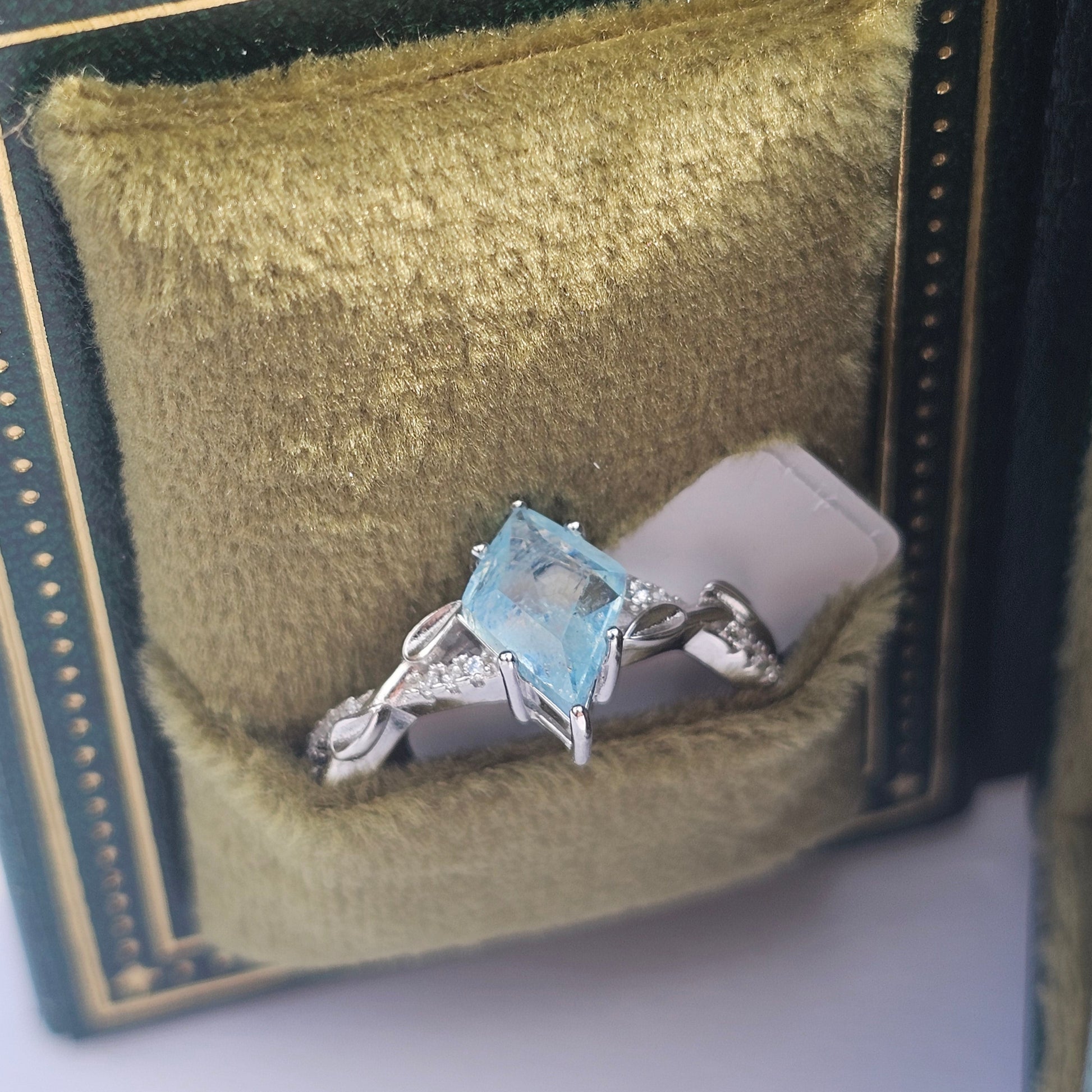Silver ring with a blue gemstone in a green jewelry box