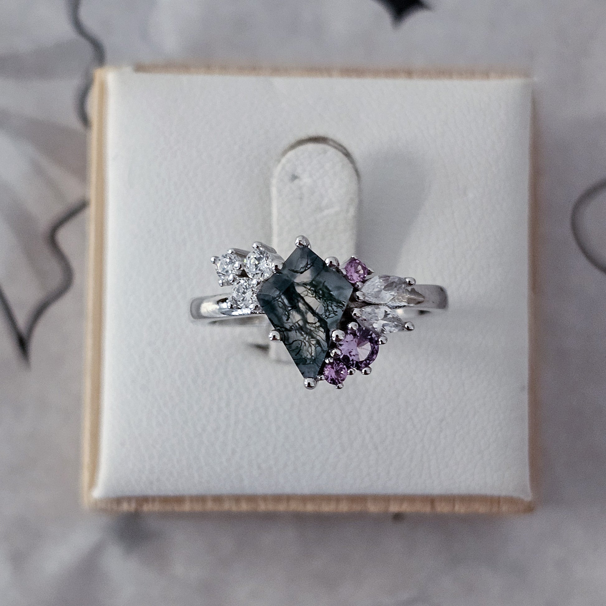 Silver ring with gemstones on a white cushion in a box